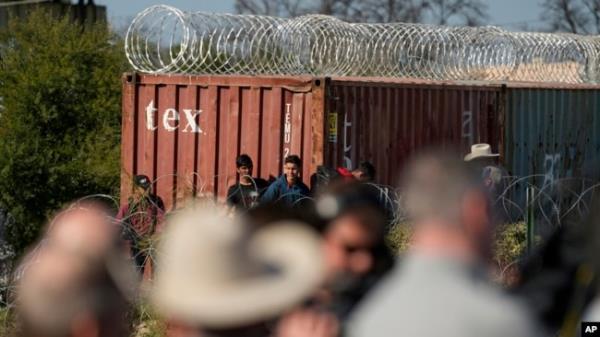 Members of Congress, bottom, look around as migrants walk near a rail car covered in co<em></em>ncertina wire at the Texas-Mexico border, in Eagle Pass, Texas, Jan. 3, 2024.