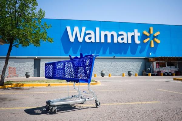 Mendoza, Argentina - January, 2020: Shopping cart on a parking lot in front of main entrance to Walmart supermarket outdoor on the street with no people. Big Walmart logo on blue background behind.