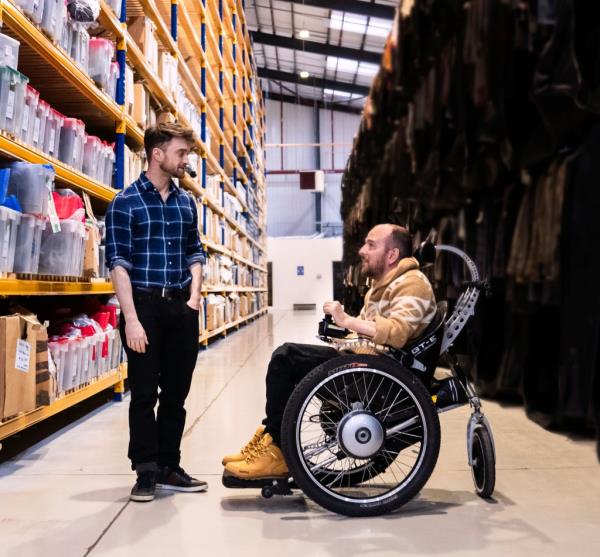 Daniel Radcliffe facing a man in a wheel chair, smiling. 