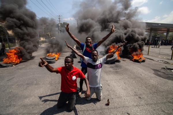 Tires burn in the streets of Port au Prince with three individuals sitting in front of them with their arms up