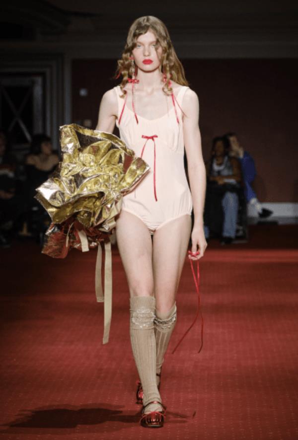 Simone Rocha model wearing cream body suit adorned with tiny, red bows paired with nude knee-high shoes