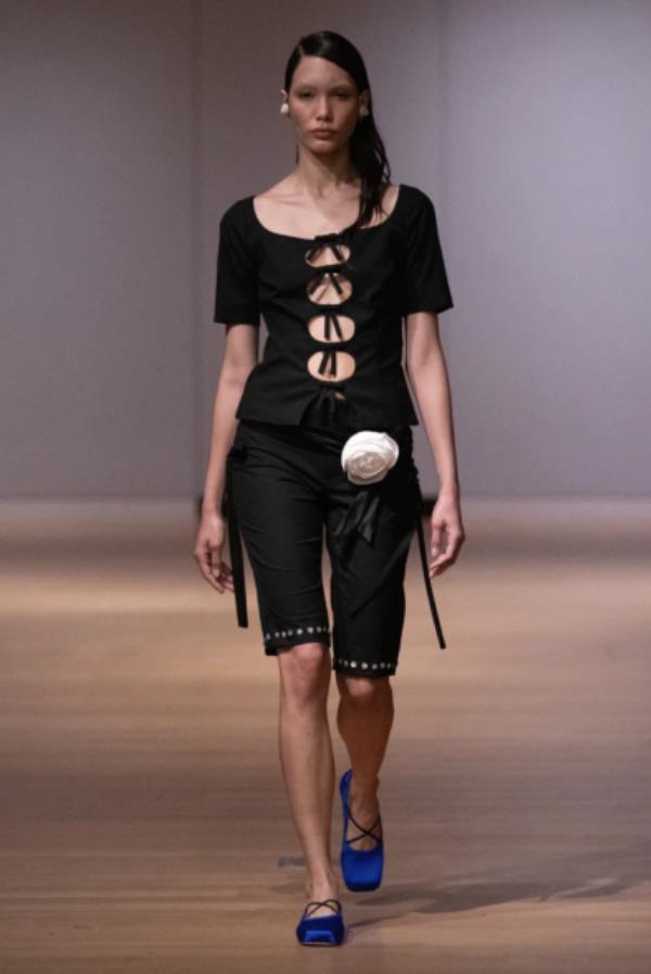 Sandy Liang model in all black top with bows down the front and knee length shorts