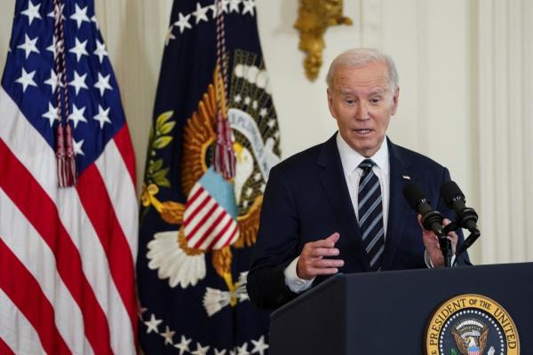 Biden stands behind a podium with his hands in the air.