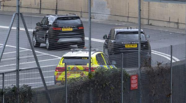 Prince Harry leaving the Windsor suite at Heathrow Terminal 5. Cars parked in a parking lot outside the terminal building.