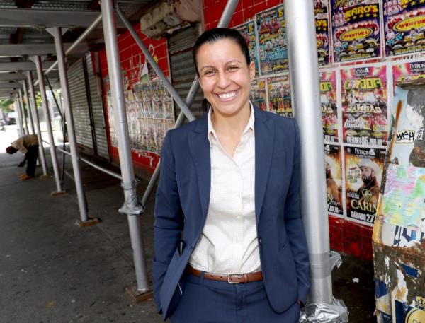 A woman in a suit running for Queens DA stands next to a wall of posters at the Natio<em></em>nal Action Network in Harlem.