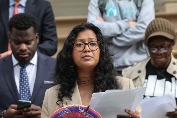 Shahana Hanif holding papers and a hat, speaking at a press co<em></em>nference critical of 