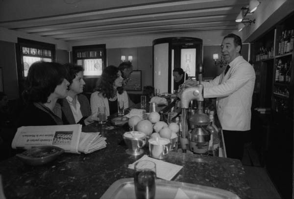 Inside Harry's Bar in Venice wher<em></em>e Giuseppe is behind the bar making drinks in a black and white photo.