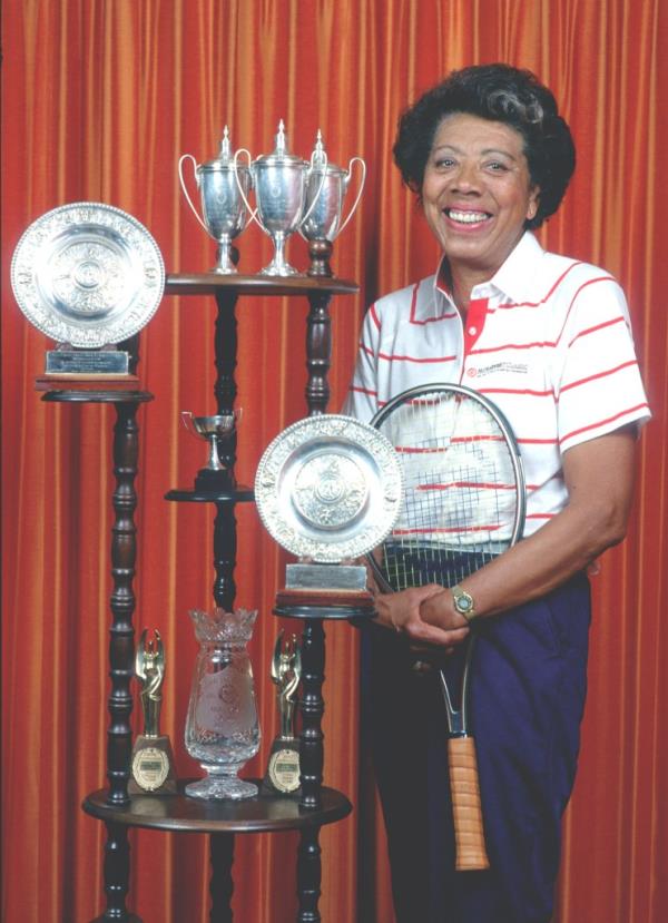 Altha Gibson posing at her home in East Orange, NJ with an impressive display of trophies. 