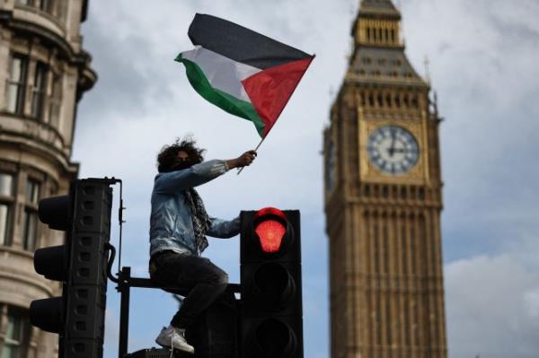 A protester waves a Palestinian flag while sitting on a set of traffic lights in Parliament Square after taking part in a 'March For Palestine' in Lo<em></em>ndon on October 28, 2023, to call for a ceasefire in the co<em></em>nflict between Israel and Hamas. Thousands of civilians, both Palestinians and Israelis, have died since October 7, 2023, after Palestinian Hamas militants ba<em></em>sed in the Gaza Strip entered southern Israel in an unprecedented attack triggering a war declared by Israel on Hamas with retaliatory bombings on Gaza. (Photo by HENRY NICHOLLS / AFP) (Photo by HENRY NICHOLLS/AFP via Getty Images)