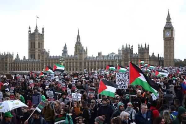 Protesters hold placards and wave Palestinian flags as they walk over Westminster Bridge with the Palace of Westminster, home of the Houses of Parliament behind during a 'March For Palestine' in Lo<em></em>ndon on October 28, 2023, to call for a ceasefire in the co<em></em>nflict between Israel and Hamas. Thousands of civilians, both Palestinians and Israelis, have died since October 7, 2023, after Palestinian Hamas militants ba<em></em>sed in the Gaza Strip entered southern Israel in an unprecedented attack triggering a war declared by Israel on Hamas with retaliatory bombings on Gaza. (Photo by HENRY NICHOLLS / AFP) (Photo by HENRY NICHOLLS/AFP via Getty Images)