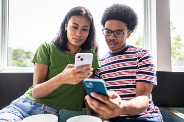 Young couple using smartpho<em></em>nes to transfer mo<em></em>ney in coffeeshop