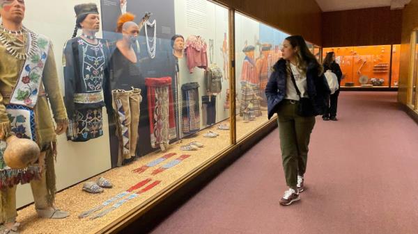 A woman looks at a display of mannequins behind glass in Native American costumes