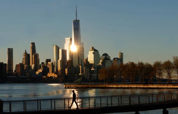 Person walking on a pier with sunrise illuminating the skyline of Lower Manhattan and One World Trade Center in New York City