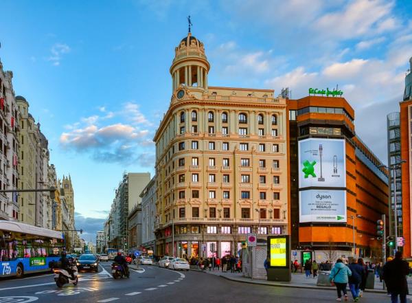 Architectural buildings and busy traffic on the Gran Via Avenue in Madrid, Spain, with people walking around