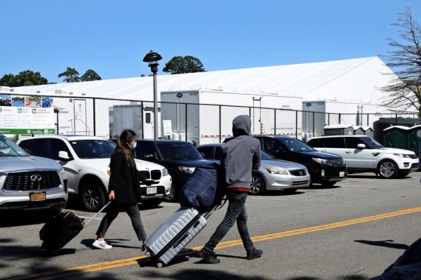 Migrants leaving the Randall Island Shelter, pulling their luggage in a parking lot, New York City, August 23, 2023.