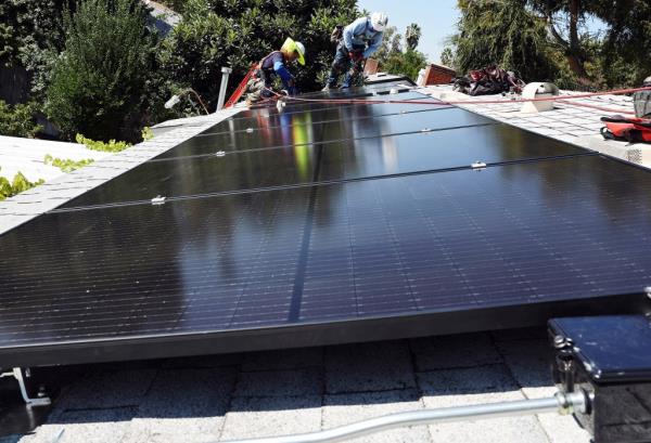 GRID Alternatives employees Tony Chang (L) and Sal Miranda install no-cost solar panels on the rooftop of a low-income household on October 19, 2023 in Pomona, California.