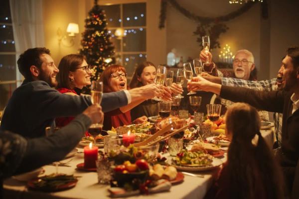 Portrait of a Handsome Young Black Man Proposing a Toast at a Christmas Dinner Table. Family and Friends Sharing Meals, Raising Glasses with Champagne, Toasting, Celebrating a Winter Holiday