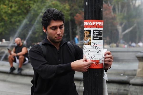 Man placing Hamas hostage poster on pole