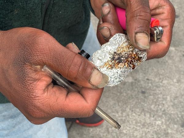 A man's hands holding a lighter, pipe, and tin foil co<em></em>ntaining fentanyl.