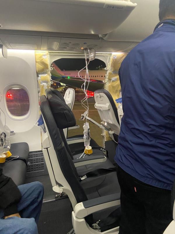 Passenger oxygen masks hang from the roof next to a missing window and a portion of a side wall of an Alaska Airlines Flight 1282.