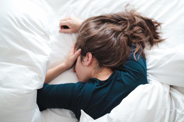 young woman in bed holding her head